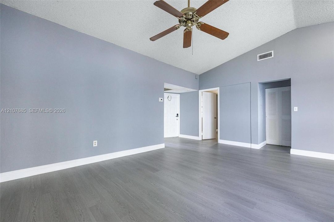 Room featuring vaulted ceilings, wood-finish flooring, and a ceiling fan with integrated lighting