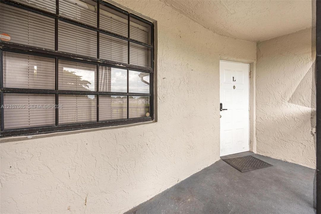 Covered entry featuring a textured stucco exterior, a single-pane glass door with a hardware lever, and a multi-lite window with a dark frame