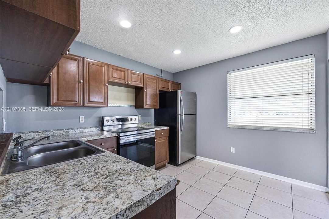 Kitchen featuring wood cabinetry, stone-finish countertops, dual-basin stainless steel sink, stainless steel range, and tile flooring