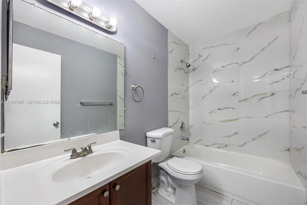 Bathroom featuring a vanity with an integrated sink, large wall-mounted mirror, light fixture with globe shades, and a shower-tub combination finished with floor-to-ceiling stone-look tile