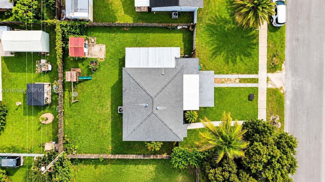 Aerial perspective featuring a lot with a fenced backyard, grass lawn, concrete driveway, and mature trees