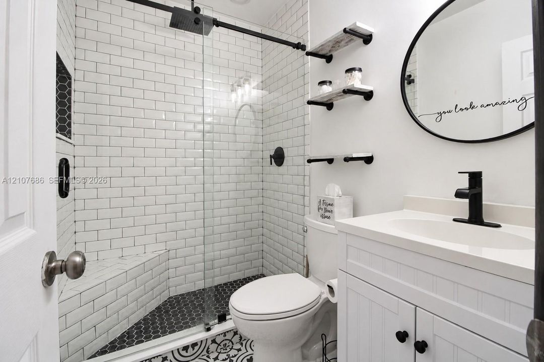 Bathroom featuring a glass-enclosed shower with white subway tile, hexagonal floor tiling, a white vanity with a single sink, matte black hardware, and wall-mounted shelving