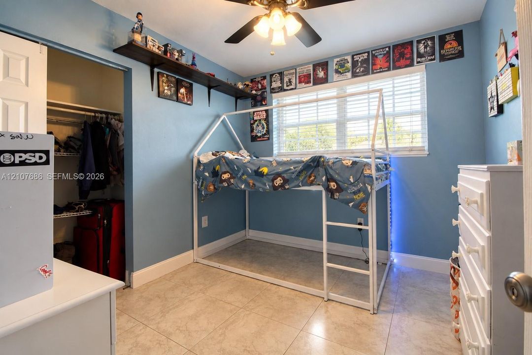 Room featuring tile flooring, ceiling fan with integrated light fixture, horizontal window blinds, and a built-in wall shelf