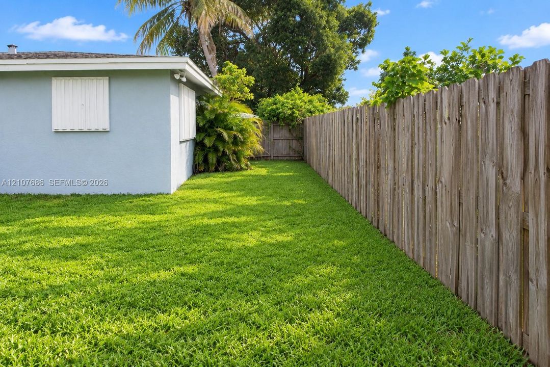 Private backyard featuring a manicured lawn, wood-panel fencing, exterior wall-mounted shutters, and mature landscaping
