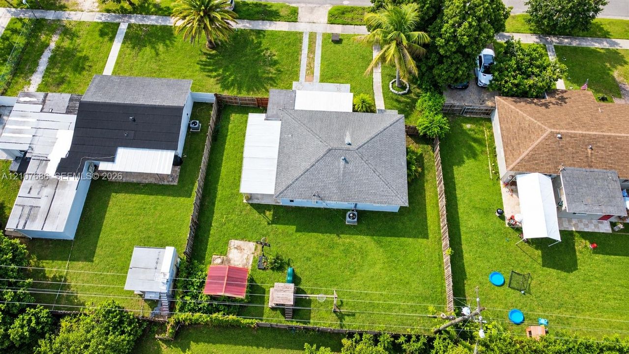 Aerial perspective of a detached residence featuring a hip roof, a concrete slab patio, a fenced backyard, and established perimeter greenery