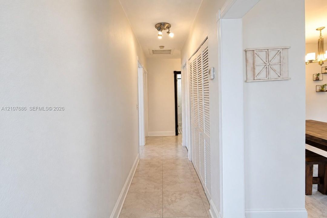 Hallway featuring neutral tile flooring, louvered closet doors, and a multi-bulb flush-mount ceiling fixture