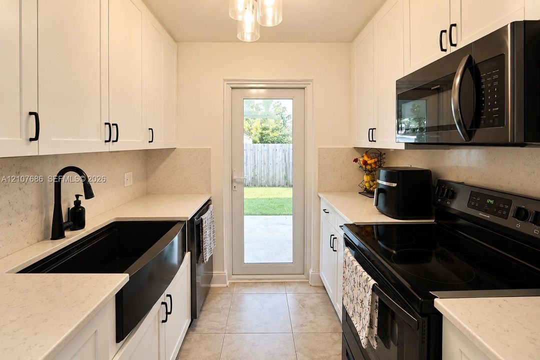Kitchen featuring white shaker-style cabinetry, solid-surface countertops, a black farmhouse sink with a matching high-arc faucet, integrated black appliances, and tile flooring