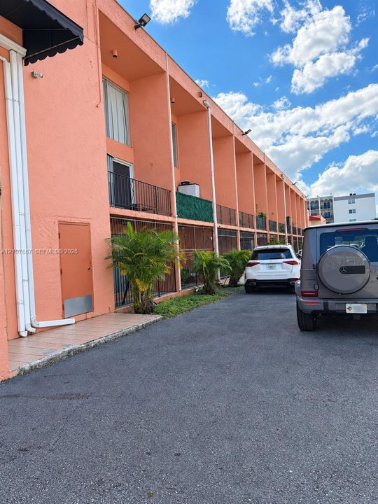 Stucco exterior building featuring multiple private balconies with metal railings, asphalt paving, and exterior wall-mounted lighting