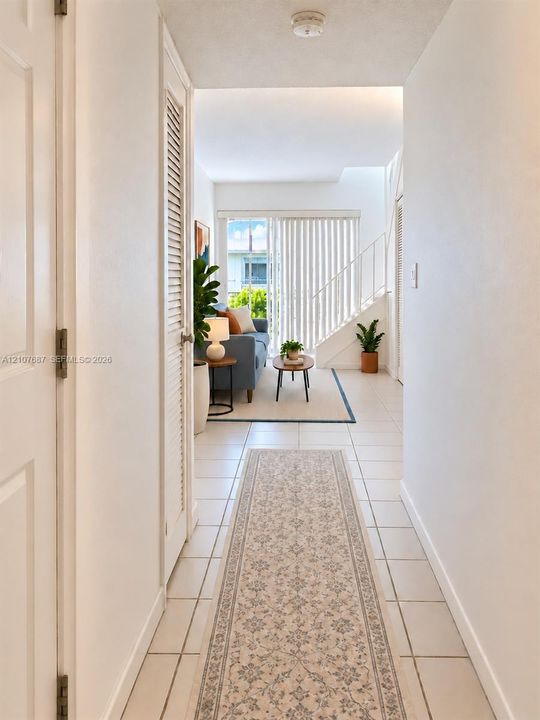 Hallway featuring neutral tile flooring, louvered closet doors, and a staircase with vertical metal railings leading toward a sliding glass door