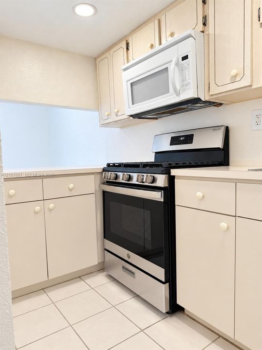 Kitchen featuring neutral-toned cabinetry, stainless steel gas range, over-the-range microwave, solid surface countertops, and tile flooring