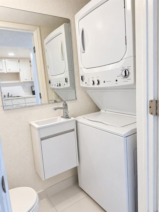 Stacked washer and dryer unit, wall-mounted vanity with rectangular sink, polished chrome faucet, and tile flooring
