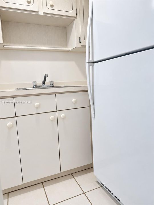 Kitchen area featuring white cabinetry, integrated sink with faucet, tiled flooring, and white refrigerator