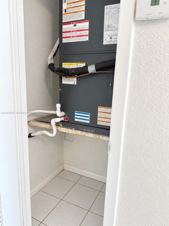 Utility closet featuring an installed HVAC air handler unit, mounted thermostat, and tiled flooring