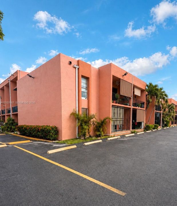 Stucco exterior building featuring covered balconies, recessed lighting, and asphalt parking area