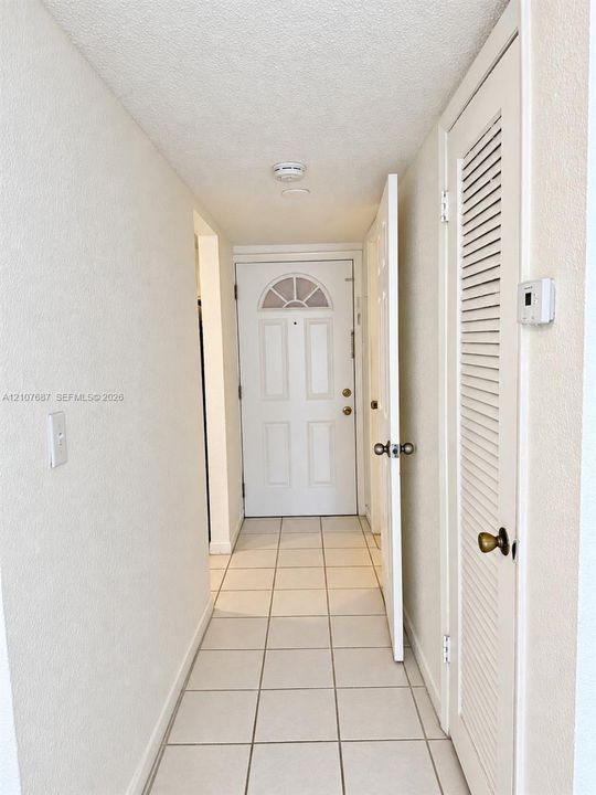 Entryway featuring a solid-core door with arched glass inlay, neutral floor tile, and a louvered closet door