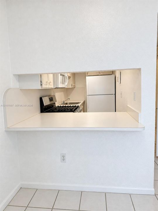 Pass-through opening with a solid-surface breakfast bar, stainless steel gas range, built-in microwave, and tile flooring