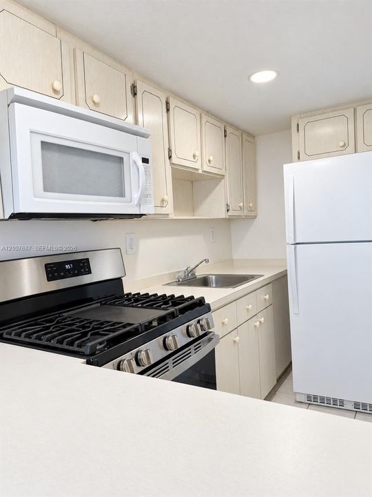 Kitchen featuring white cabinetry, stainless steel gas range, over-the-range microwave, white refrigerator, and solid surface countertop with integrated sink
