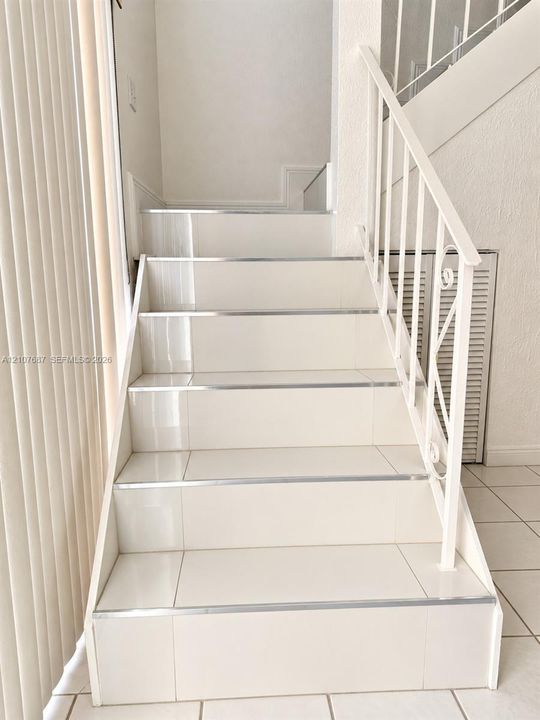 Staircase featuring glossy tile steps, metallic trim edges, and a white decorative metal railing