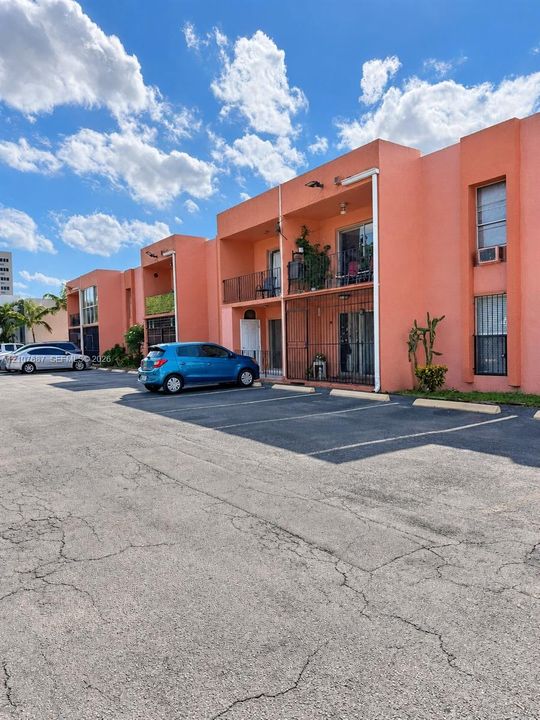 Stucco exterior building featuring multiple balconies with metal railings and paved surface parking