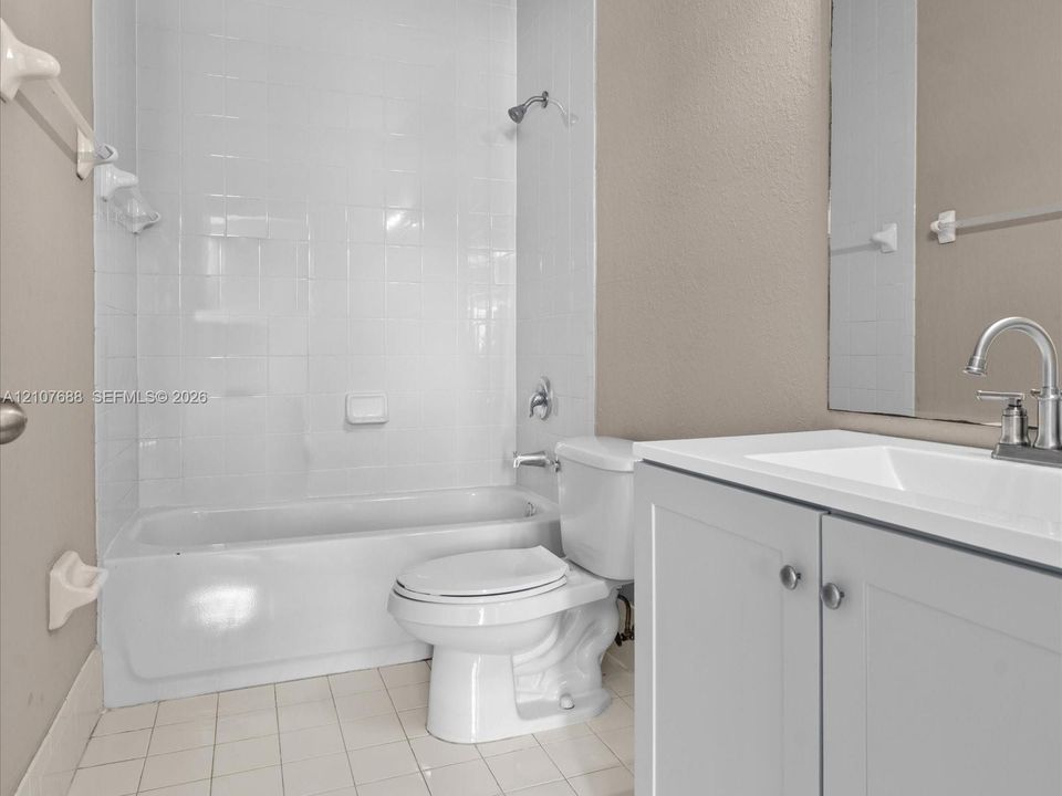 Bathroom featuring a white porcelain tub with tiled surround, a vanity with a white countertop and basin, chrome faucet hardware, and tile flooring