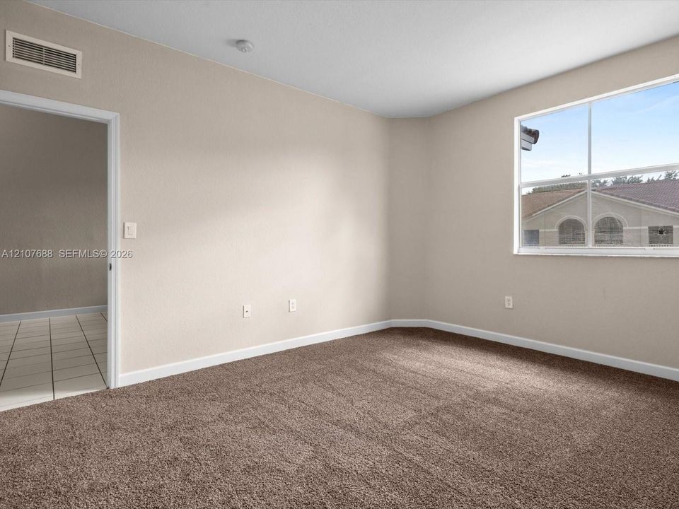 Neutral-toned interior room featuring wall-to-wall carpeting, a single-pane window, and an arched-top doorway leading to a tiled-floor area