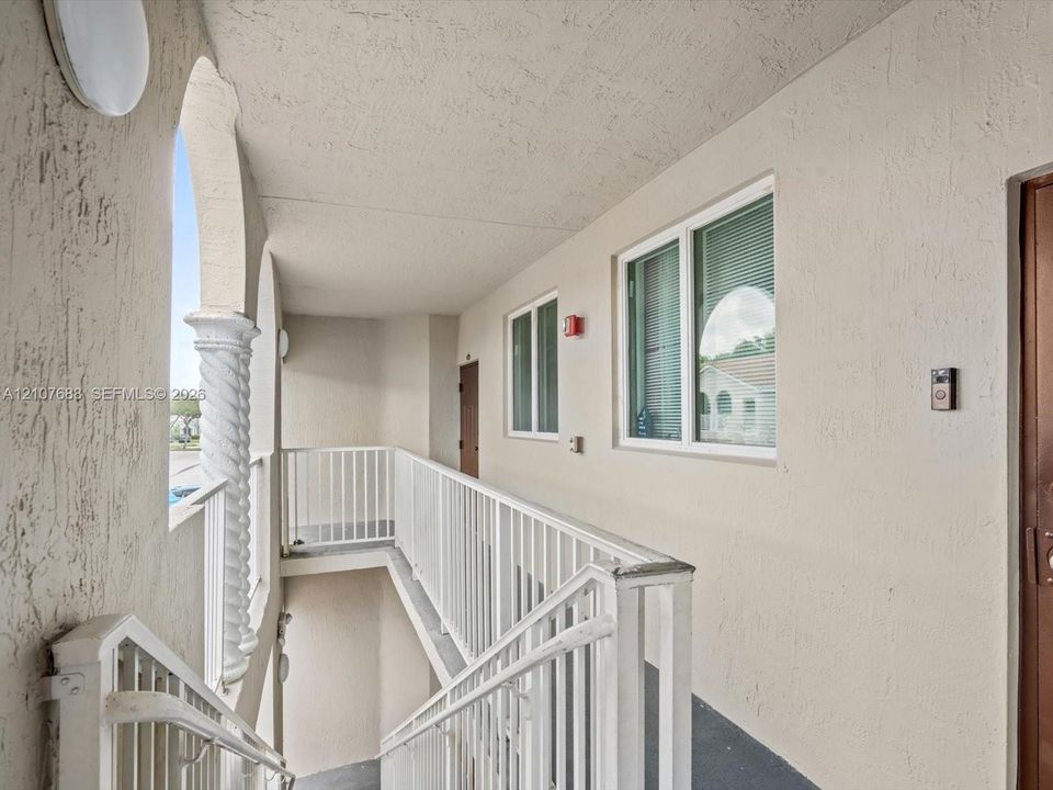 Exterior walkway featuring stucco walls, a decorative spiral column, and white metal railings