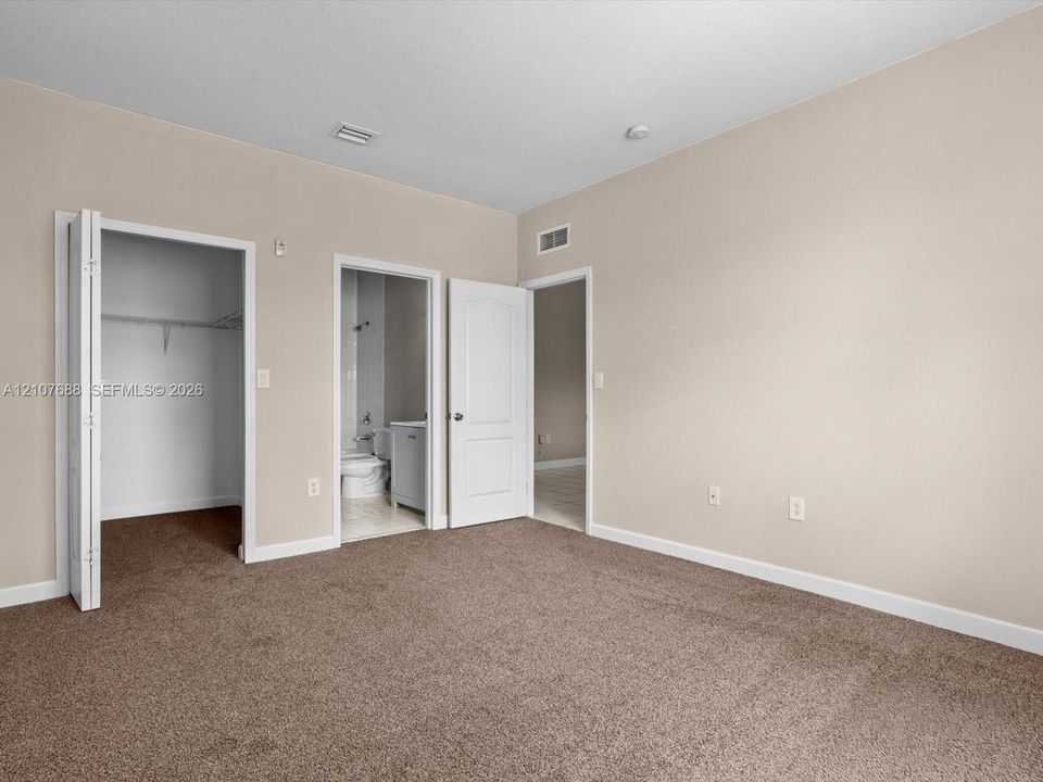 Neutral-toned interior featuring wall-to-wall carpeting, multiple interior doorways, a built-in reach-in closet with shelving, and a separate doorway to a tiled bathroom