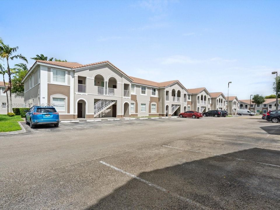Two-story building featuring stucco exterior, clay tile roof, arched entryway accents, and dedicated surface parking