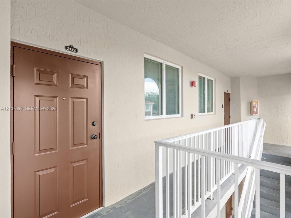 Paneled entry door with hardware, neutral exterior wall finish, white metal railing, and dual-pane windows