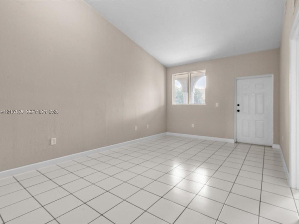 Interior space featuring vaulted ceilings, light-toned ceramic tile flooring, neutral wall paint, and a white six-panel exterior entry door