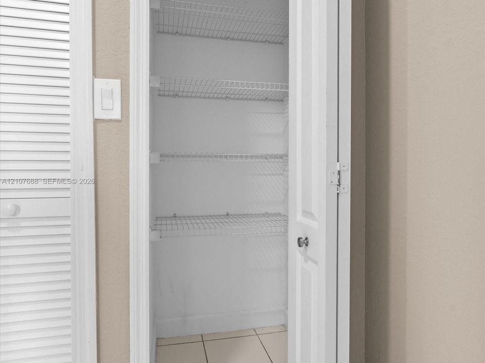 Storage closet featuring white six-panel door, white wire shelving, and tile flooring