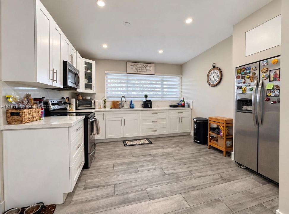 Kitchen featuring white shaker-style cabinetry, light-toned stone countertops, recessed lighting, and wood-finish flooring