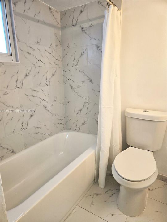 Full bathroom featuring a white bathtub, floor-to-ceiling large-format tile surround with a veined pattern, and matching tile flooring