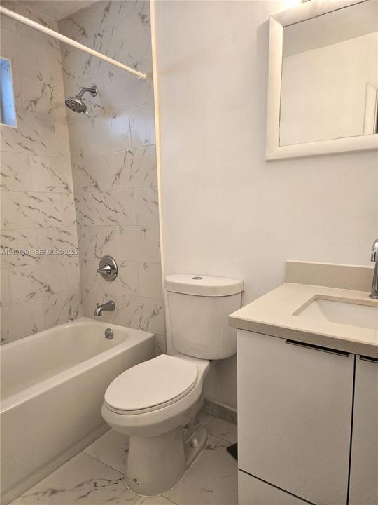 Bathroom featuring a shower-tub combination with white patterned tile surround, vanity with an integrated countertop sink, chrome plumbing fixtures, and wall-mounted mirror