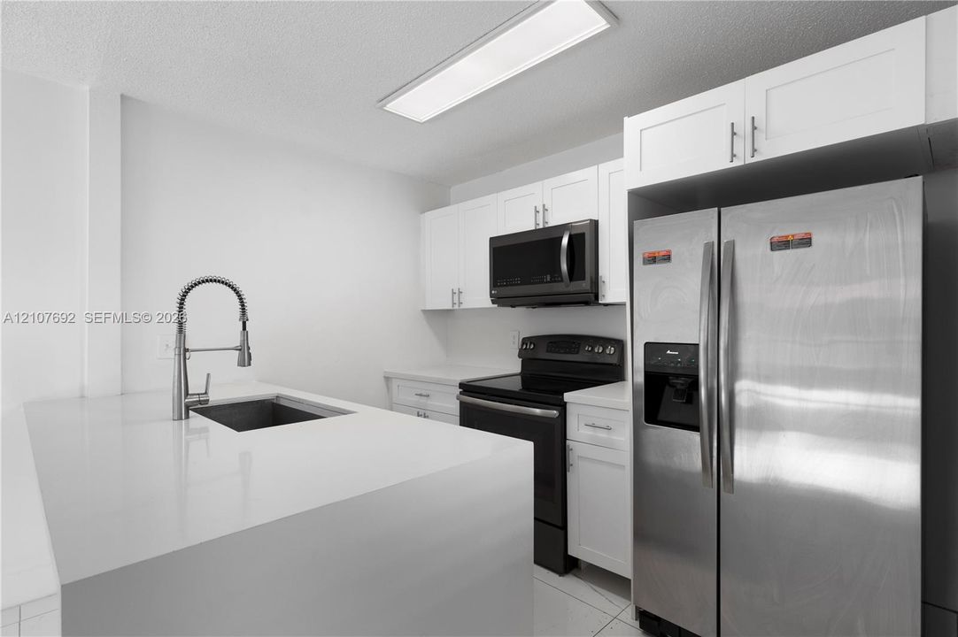 Kitchen featuring white cabinetry, quartz countertops, a stainless steel undermount sink with a pull-down sprayer faucet, and stainless steel appliances
