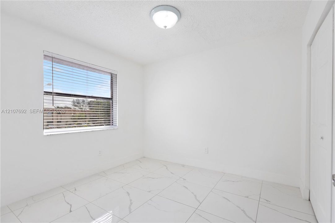 Room featuring white walls, large-format tile flooring with veining, a single-pane window with horizontal blinds, and a built-in closet with panel doors