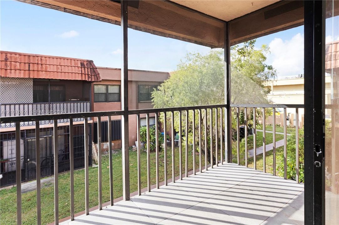 Screened-in balcony featuring a metal railing, concrete flooring, and an overhang