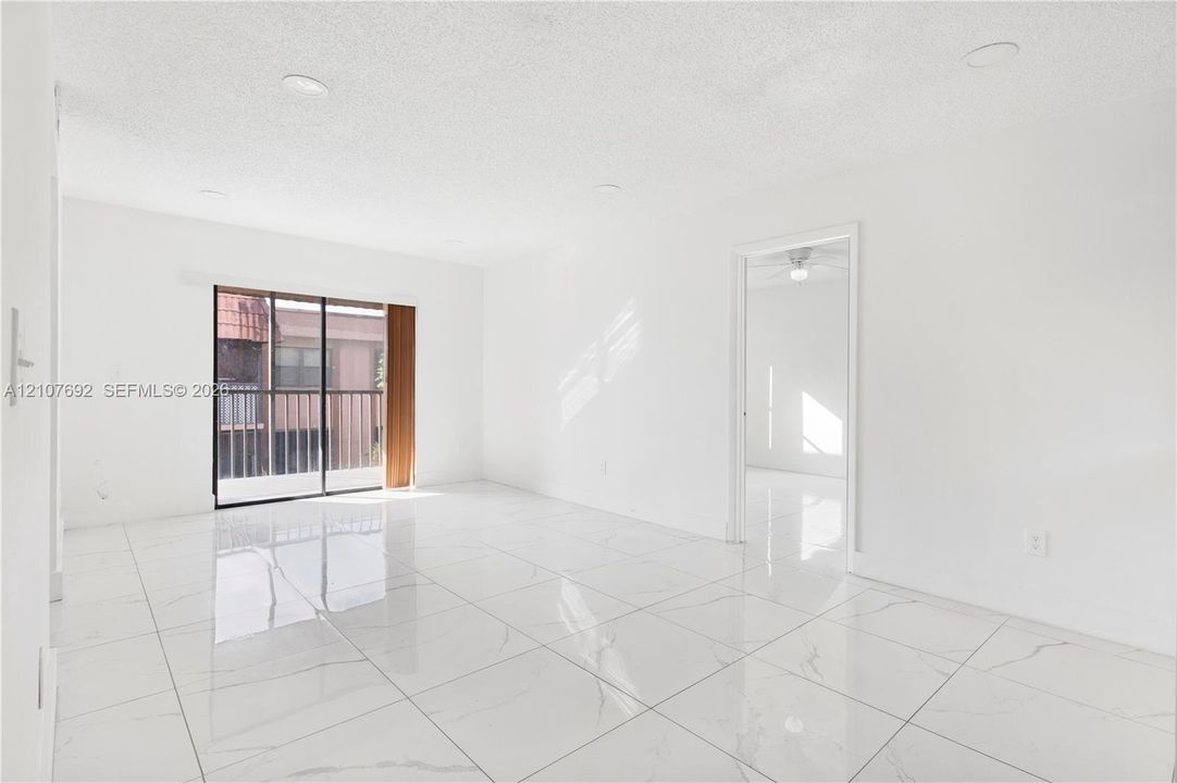 Large-format polished tile flooring, recessed ceiling lighting, sliding glass door with balcony access, and crisp white wall finishes