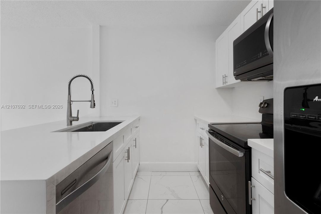 Kitchen featuring white cabinetry, quartz countertops, undermount sink with a high-arch pull-down faucet, stainless steel dishwasher, and large-format tile flooring