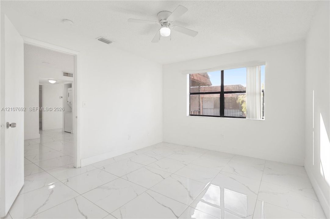 Neutral-toned interior featuring large-format tile flooring with marble-style veining, a white ceiling fan with integrated lighting, and a window with a black frame