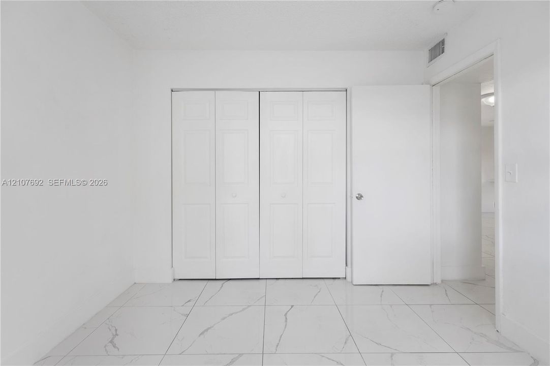 Interior space featuring large-format white tile flooring with grey veining, crisp white wall finishes, and a four-panel bi-fold closet door
