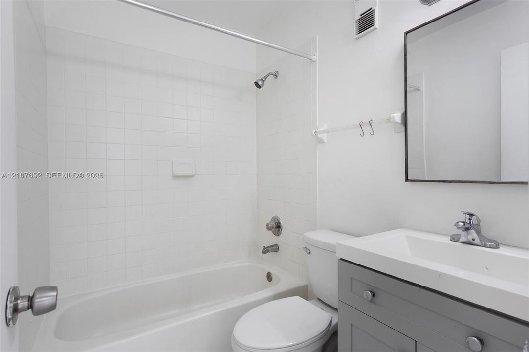 Bathroom featuring a gray shaker-style vanity, white integrated countertop sink, framed wall mirror, and tub-shower combination with white tile surround
