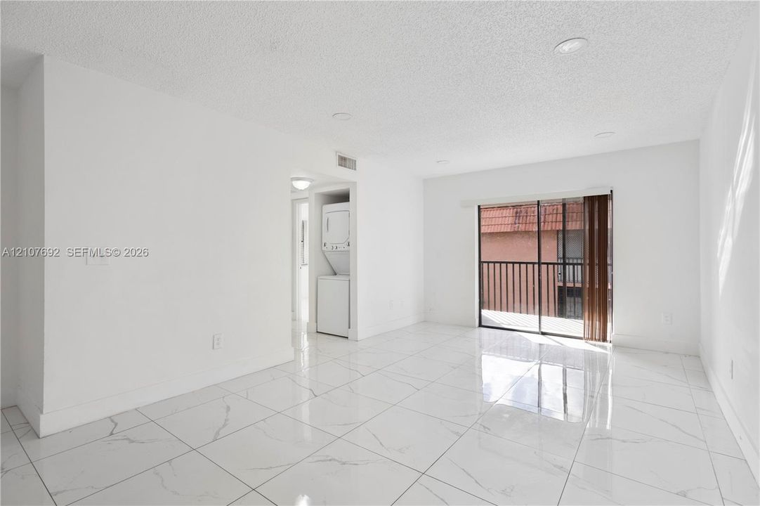 Large-format tile flooring, recessed ceiling lighting, sliding glass door with external balcony access, and stacked laundry unit