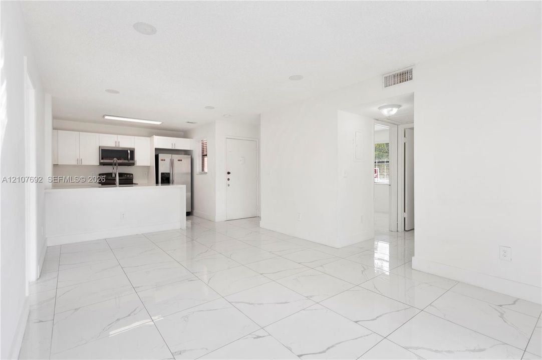 Large-format polished tile flooring, white cabinetry, integrated stainless steel appliances, recessed lighting, and a breakfast bar