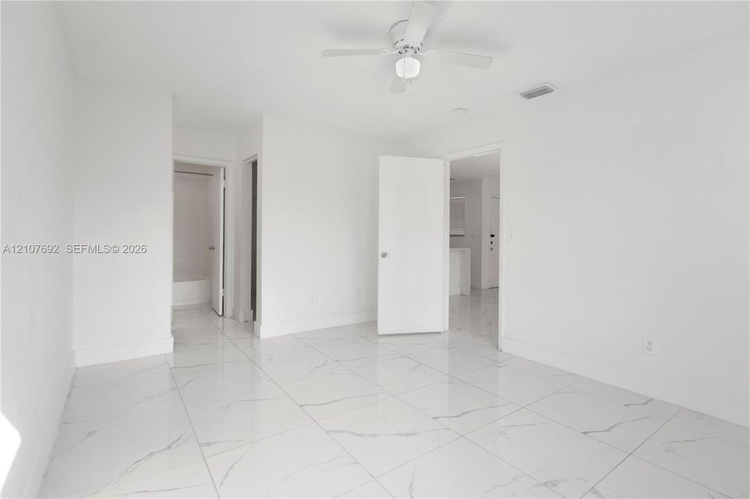 Bright interior room featuring large-format tile flooring with veining, white wall finishes, and a ceiling-mounted fan with integrated light