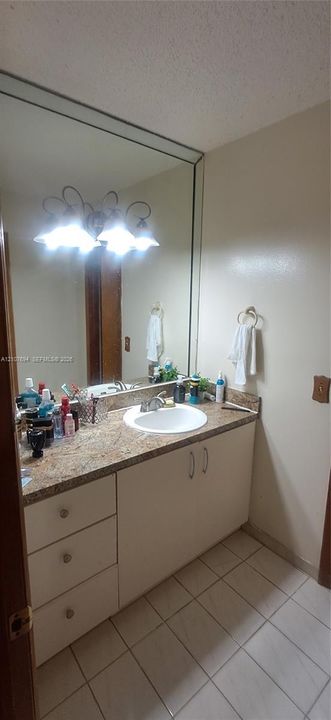 Bathroom vanity featuring solid-surface countertop with integrated oval sink, base cabinetry with three drawers, large wall-mounted mirror, and tile flooring