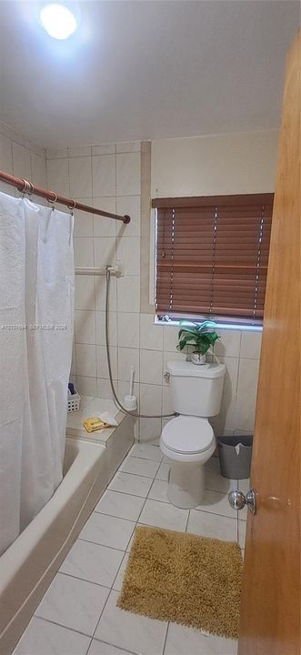 Full-height ceramic tile wall surround, integrated bathtub, ceramic tile flooring, and horizontal window blinds