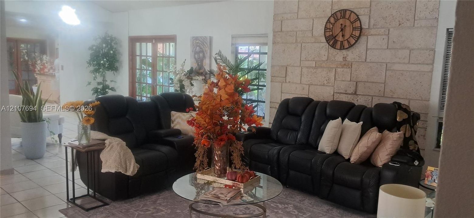 Living area featuring a floor-to-ceiling natural stone accent wall, light-toned ceramic tile flooring, and French doors