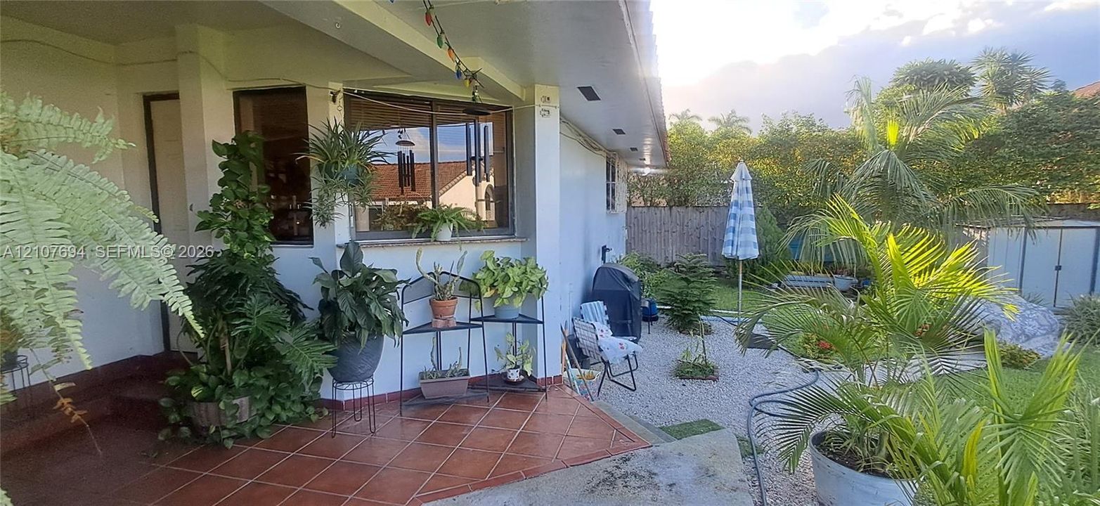 Covered patio featuring terracotta-style tile flooring, gravel ground cover, and mature exterior landscaping