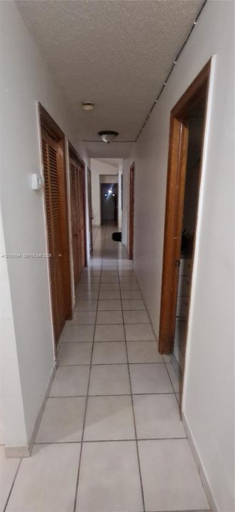 Hallway featuring neutral-toned tile flooring, louvered wood-finish closet doors, and flush-mount lighting fixtures